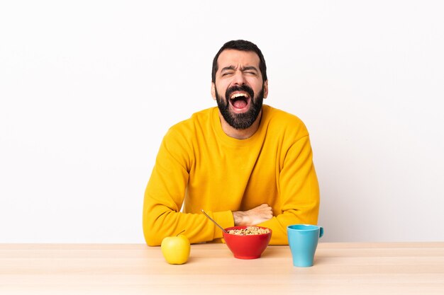 Homme caucasien prenant son petit déjeuner dans une table en criant à l'avant avec la bouche grande ouverte.