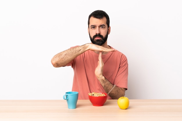 Homme caucasien prenant son petit déjeuner dans une table faisant le geste du temps.