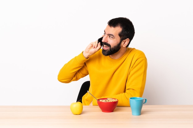 Homme caucasien prenant son petit déjeuner dans une table en gardant une conversation avec le téléphone mobile avec quelqu'un