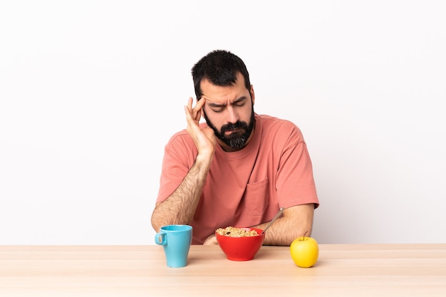 Homme caucasien prenant son petit déjeuner dans une table avec des maux de tête.