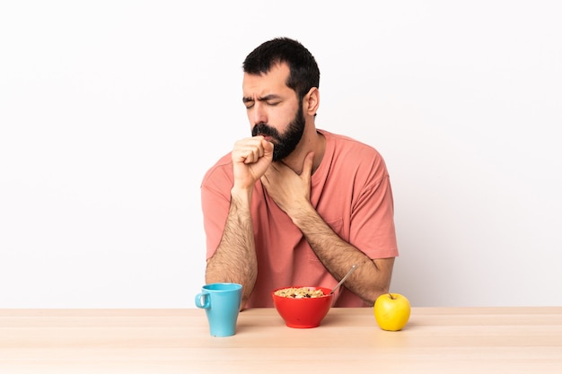 Homme caucasien prenant son petit déjeuner dans une table toussant beaucoup