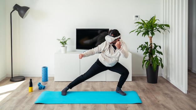 Homme caucasien profitant de lunettes de réalité virtuelle Étudiant de Wushu dans un vêtement de sport jouant à un jeu vidéo sur le salon confortable maison Guy faisant des gestes et utilisant un casque vr pour s'entraîner aux arts conjugaux de Kungfu