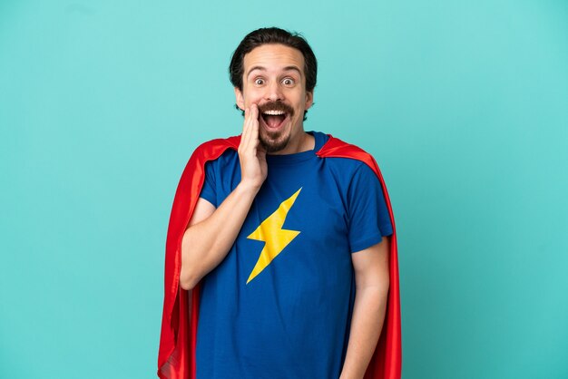 Homme caucasien de super héros isolé sur fond bleu avec une expression faciale surprise et choquée