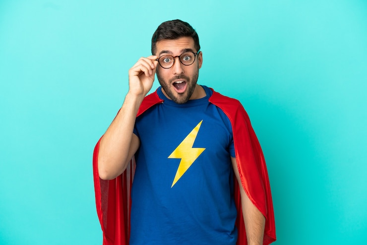 Photo homme caucasien de super héros isolé sur fond bleu avec des lunettes et surpris