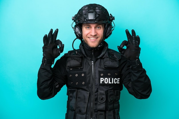 Homme caucasien SWAT isolé sur fond bleu montrant un signe ok avec les doigts