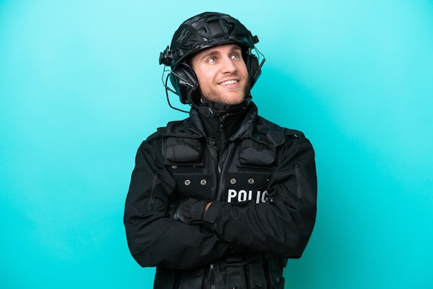 Homme caucasien SWAT isolé sur fond bleu regardant en souriant