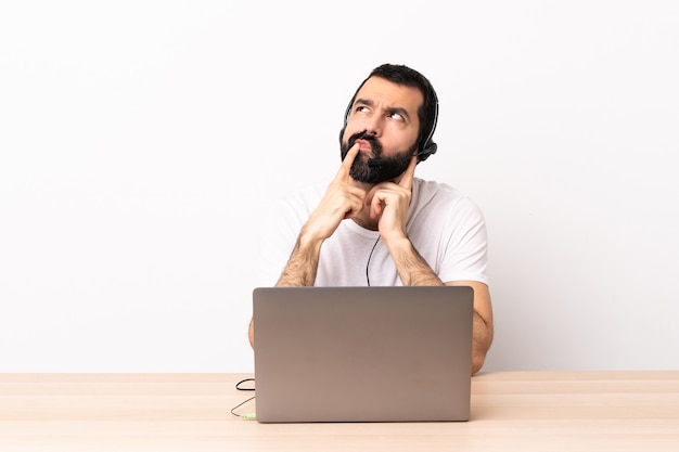 Homme caucasien de télévendeur travaillant avec un casque et avec un ordinateur portable ayant des doutes tout en levant les yeux.