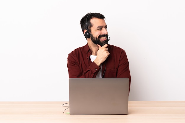 Homme caucasien de télévendeur travaillant avec un casque et avec un ordinateur portable à la recherche sur le côté et souriant.