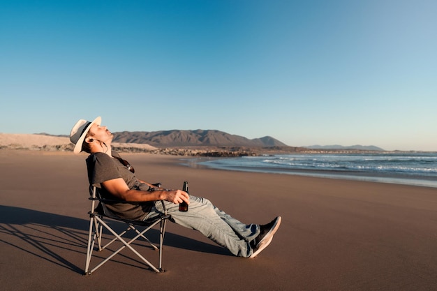 Homme en chaise de camping sur la plage avec une boisson non alcoolisée ou une bière relaxante au coucher du soleil