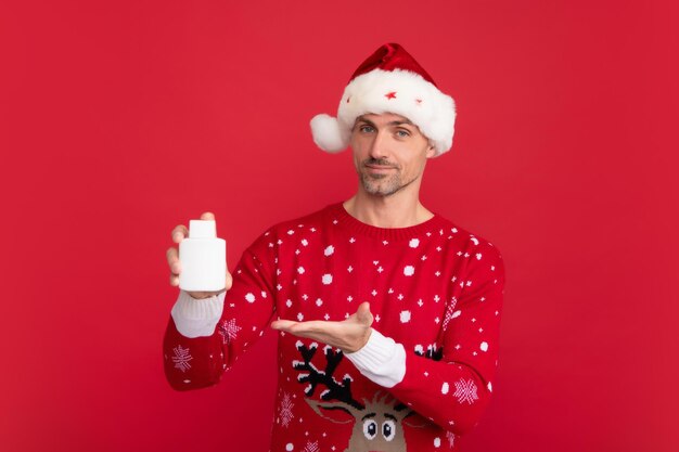 L'homme en chandail de Noël et un chapeau tiennent une bouteille de médicament sur un fond de couleur