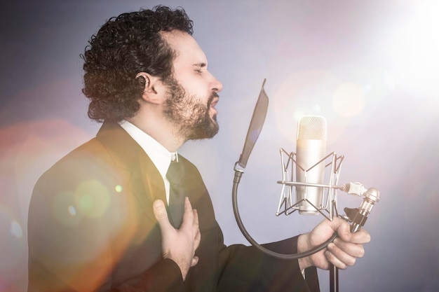 homme chanteur avec costume noir et microphone sur fond avec rideau rouge