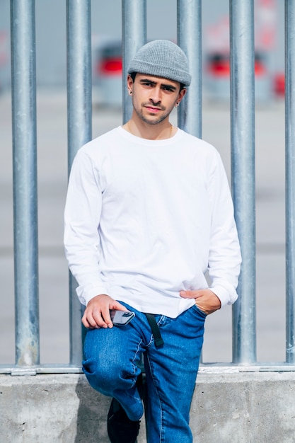 Homme avec chapeau, jeans et t-shirt blanc posant sur rue