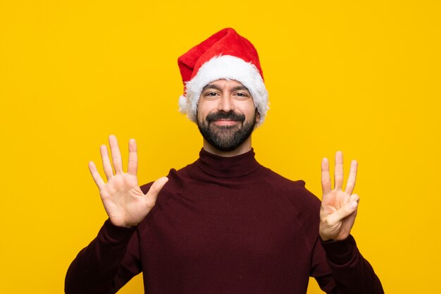 Homme avec chapeau de Noël sur mur jaune isolé comptant huit avec les doigts