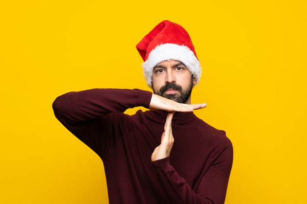 Homme avec un chapeau de Noël sur mur jaune isolé, geste de délai d'expiration