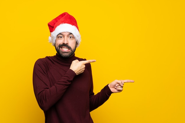 Homme avec chapeau de Noël pointant vers le côté sur fond jaune isolé