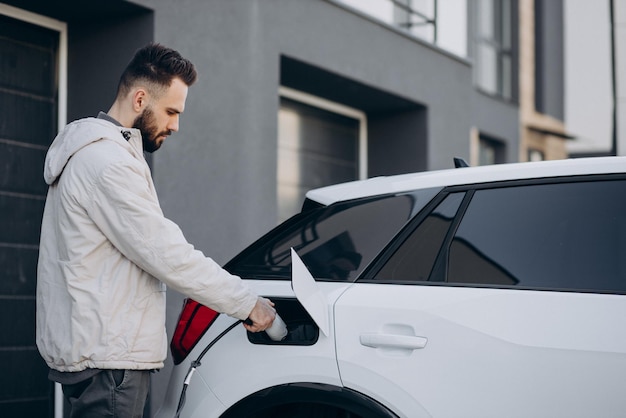 Homme chargeant une voiture électrique près de la maison