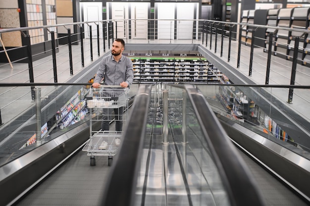 Un homme avec un chariot d'achat sur un escalier mécanique dans un magasin de quincaillerie