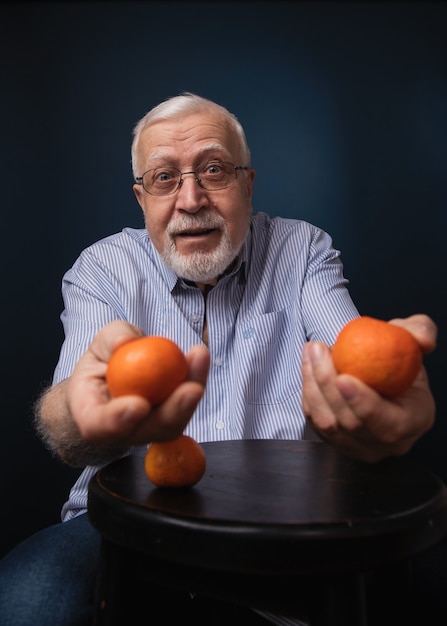 Homme charismatique en âge et à lunettes, étend ses mains dans le cadre avec des mandarines orange,