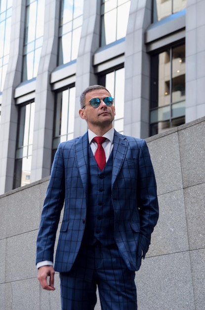 Homme charismatique en costume à carreaux dans le contexte d'un bureau de centre d'affaires Un employé élégant dans des lunettes de miroir tendance exhale la confiance, la force et le professionnalisme