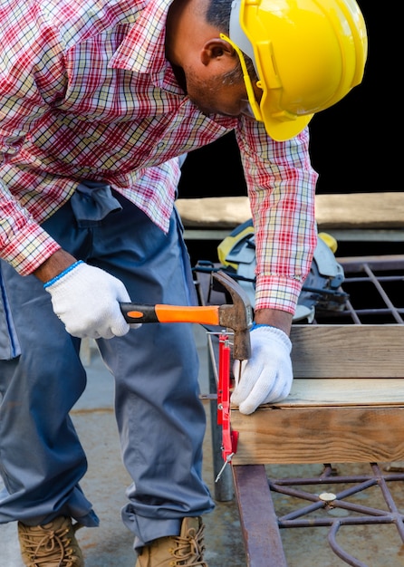 Homme charpentier à l'aide d'un marteau pour enfoncer un clou dans une planche de bois. Outils et équipements pour le concept de travail du bois.