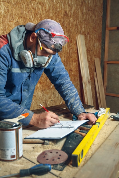 Photo homme charpentier dans son home studio travaillant avec du bois et dessine des croquis au crayon dans un cahier