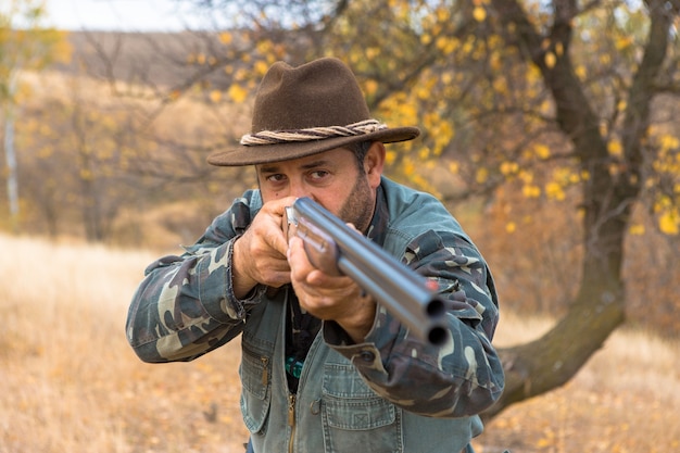 Homme chasseur en tenue de camouflage avec une arme à feu pendant la chasse à la recherche d'oiseaux sauvages ou de gibier. Saison de chasse d'automne.