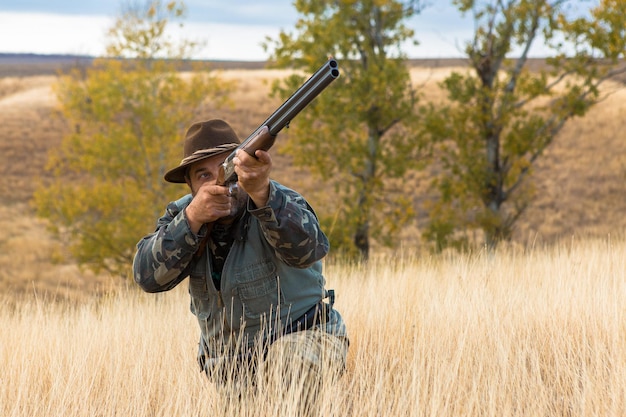 Homme chasseur en tenue de camouflage avec une arme à feu pendant la chasse à la recherche d'oiseaux sauvages ou de gibier