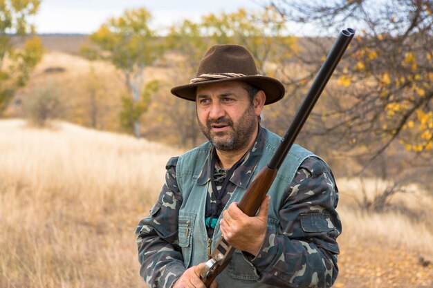 Homme chasseur en tenue de camouflage avec une arme à feu pendant la chasse à la recherche d'oiseaux sauvages ou de gibier