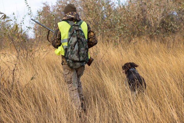 Homme chasseur en tenue de camouflage avec une arme à feu pendant la chasse à la recherche d'oiseaux sauvages ou de gibier