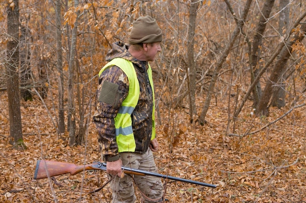 Homme chasseur en tenue de camouflage avec une arme à feu pendant la chasse à la recherche d'oiseaux sauvages ou de gibier