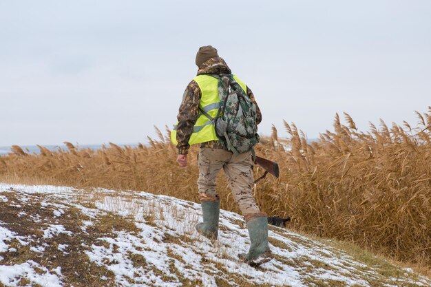 Homme chasseur en tenue de camouflage avec une arme à feu pendant la chasse à la recherche d'oiseaux sauvages ou de gibier