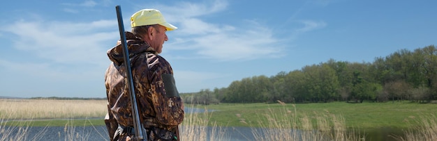 Homme chasseur en tenue de camouflage avec une arme à feu pendant la chasse à la recherche d'oiseaux sauvages ou de gibier