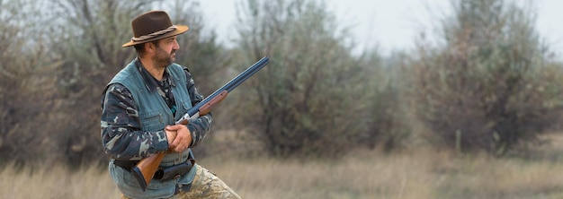 Homme chasseur en tenue de camouflage avec une arme à feu pendant la chasse à la recherche d'oiseaux sauvages ou de gibier