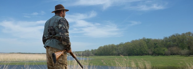 Homme chasseur en tenue de camouflage avec une arme à feu pendant la chasse à la recherche d'oiseaux sauvages ou de gibier