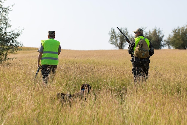 Homme chasseur en tenue de camouflage avec une arme à feu pendant la chasse à la recherche d'oiseaux sauvages ou de gibier