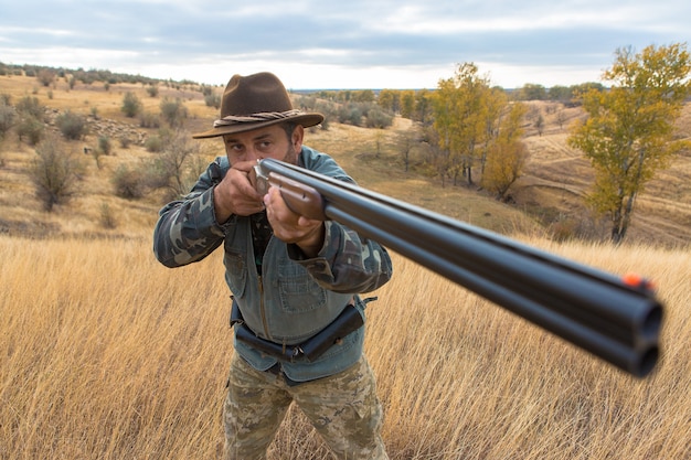 Homme chasseur en tenue de camouflage avec une arme à feu pendant la chasse à la recherche d'oiseaux sauvages ou de gibier