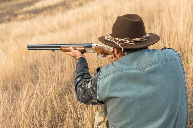 Photo homme chasseur en tenue de camouflage avec une arme à feu pendant la chasse à la recherche d'oiseaux sauvages ou de gibier