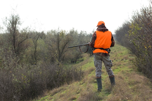 Homme chasseur en tenue de camouflage avec une arme à feu pendant la chasse à la recherche d'oiseaux sauvages ou de gibier