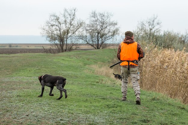 Homme chasseur en tenue de camouflage avec une arme à feu pendant la chasse à la recherche d'oiseaux sauvages ou de gibier