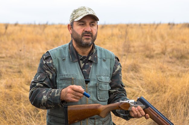 Homme chasseur en tenue de camouflage avec une arme à feu pendant la chasse à la recherche d'oiseaux sauvages ou de gibier