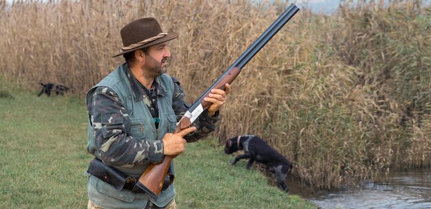 Homme chasseur en tenue de camouflage avec une arme à feu pendant la chasse à la recherche d'oiseaux sauvages ou de gibier