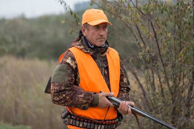 Homme chasseur en tenue de camouflage avec une arme à feu pendant la chasse à la recherche d'oiseaux sauvages