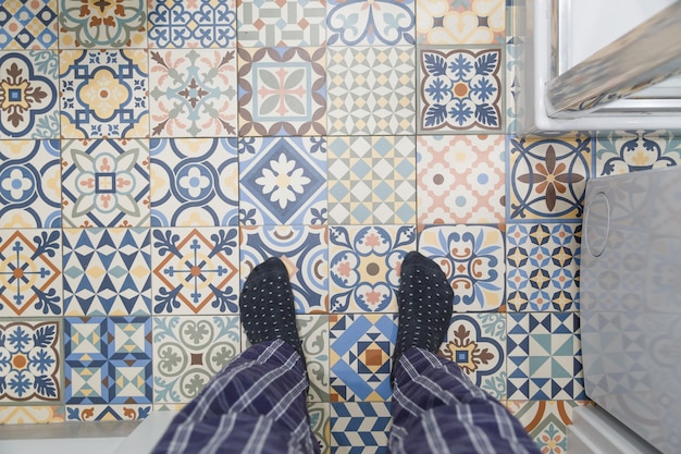 Photo l'homme en chaussettes chaudes se dresse sur un sol de salle de bains carrelée en céramique froide
