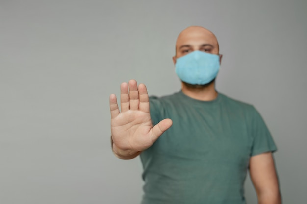 homme chauve d'âge moyen dans un masque médical et un T-shirt montre un panneau d'arrêt avec sa main