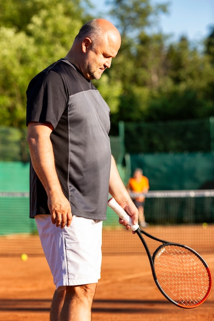 Un homme chauve d'âge moyen joue au tennis sur le terrain extérieur. Journée ensoleillée