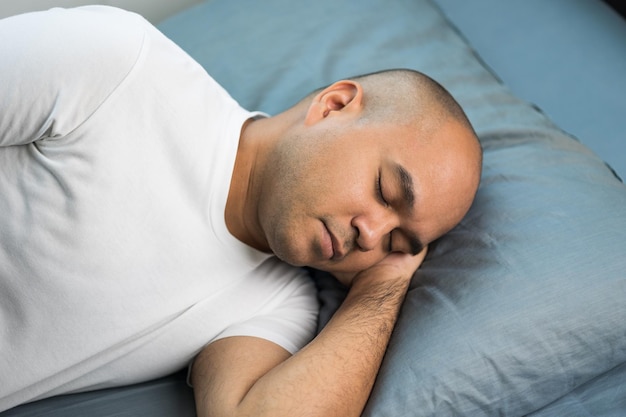 Un homme chauve asiatique d'environ 30 ans en t-shirt blanc dort