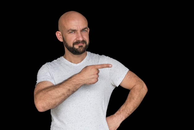 Homme chauve blanc avec une barbe dans un t-shirt blanc pointe le doigt sur le côté