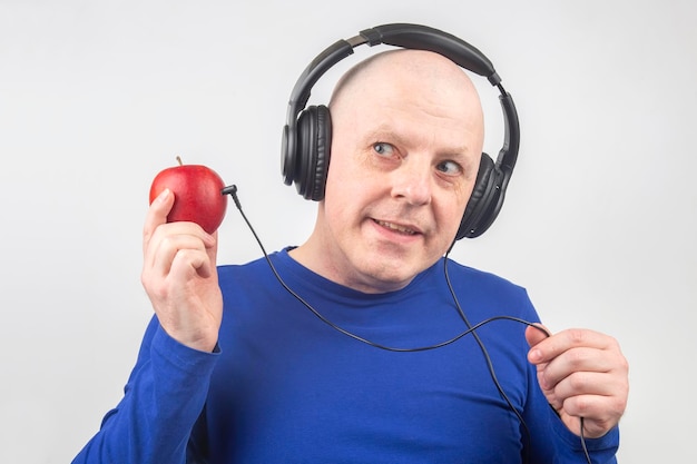 Un homme chauve avec un casque écoute de la musique via un lecteur de pomme rouge Métaphore et concept d'avantages vitaminiques dans la musique et le son