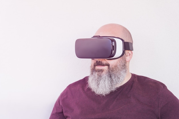 Homme chauve avec grosse barbe portant des lunettes de réalité virtuelle ou t-shirt marron sur mur blanc