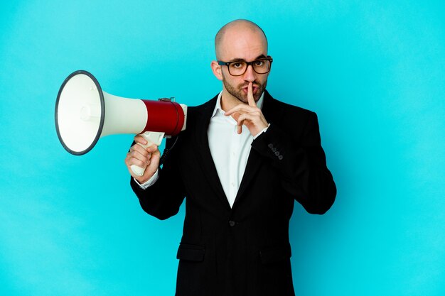 Homme chauve jeune entreprise tenant un mégaphone isolé gardant un secret ou demandant le silence.